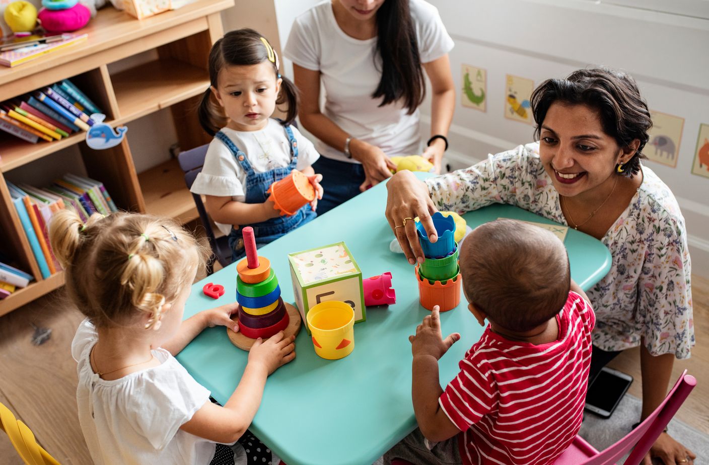 Zwei Erzieherinnen spielen mit Kindern an einem Kindertisch mit Holzspielzeug. 