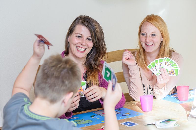Zwei Erzieherinnen spielen mit einem Kind Karten und haben Spaß dabei. 