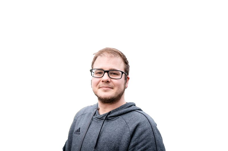 Ein junger Mann mit Bart und Brille lächelt. Er strahlt Ruhe und Empathie aus.