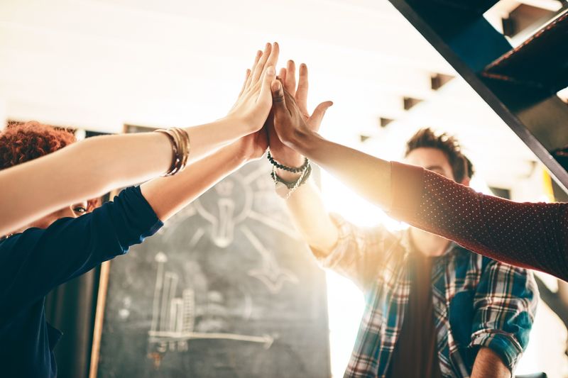 Eine Gruppe von Menschen stehen im Kreis und legen ihre Hände gemeinsam in die Mitte – ein starkes Symbol für Teamgeist und Zusammenhalt.