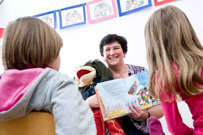 Eine ältere Frau liest zwei Kindern aus einem Buch vor.