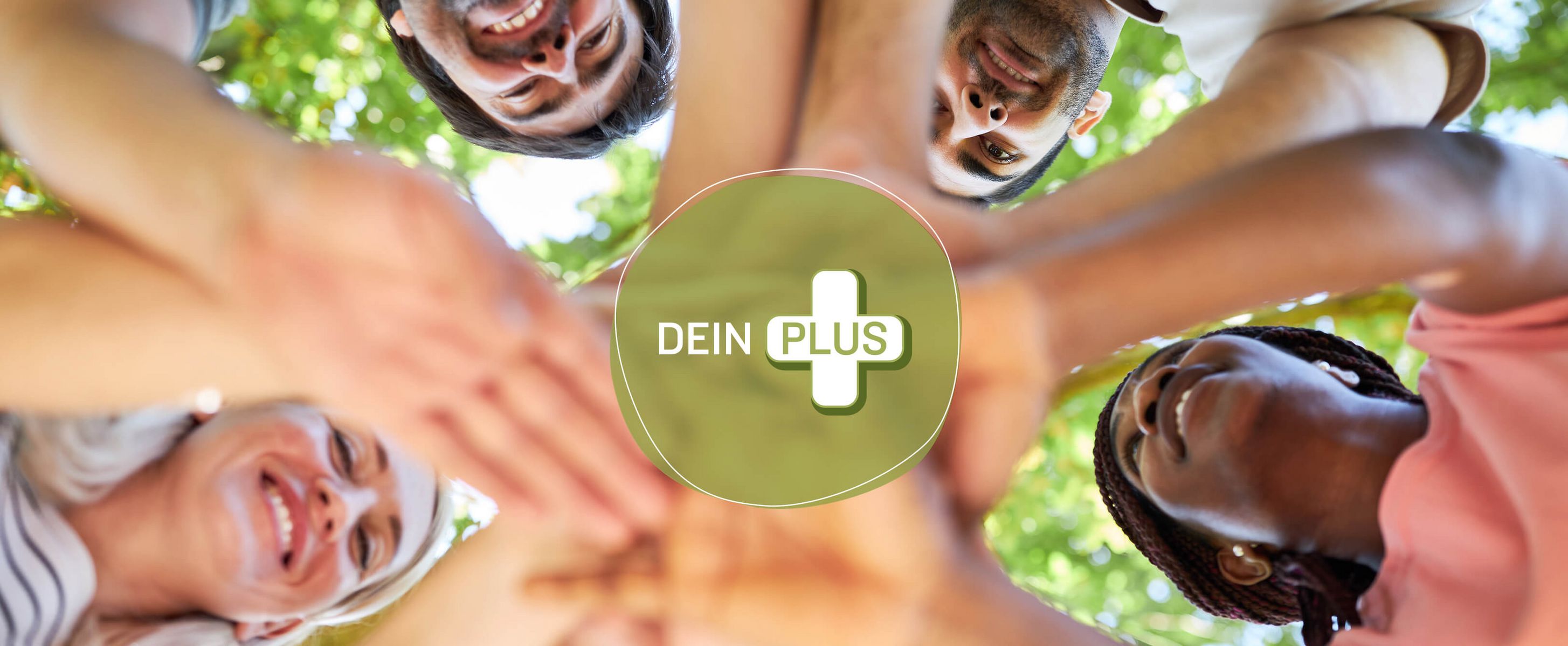 Eine diverse Gruppe von Menschen stehen im Kreis, lächeln einander an und legen ihre Hände gemeinsam in die Mitte – ein starkes Symbol für Zusammenhalt, Teamgeist und Vertrauen. In der Mitte steht das Logo „DEIN PLUS“.