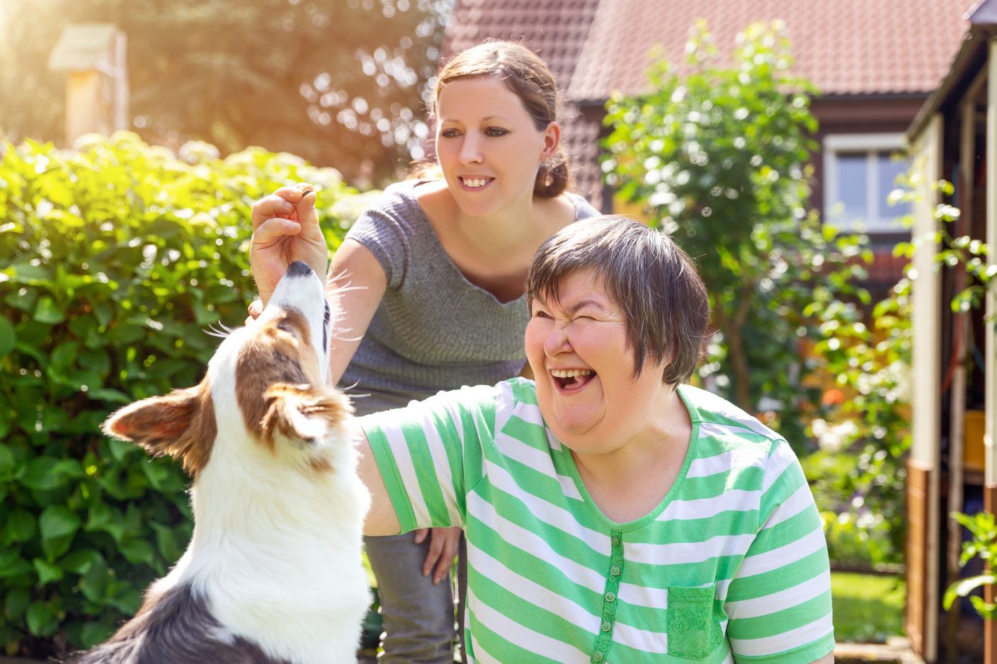 Eine Heilpädagogin und eine Frau mit Behinderung geben einem Hund ein Leckerchen. 