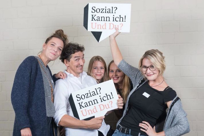 Eine lustige Gruppe von Menschen halten Schilder hoch mit der Aufschrift: "Sozial? Kann ich! Und du?".
